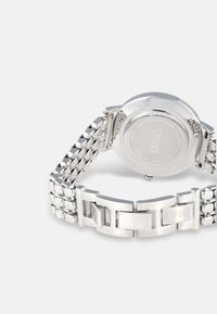 Orologio in acciaio inossidabile argento con cassa rotonda e bracciale a maglie. Presenta una fibbia e un retro liscio. Testo visibile sul retro.