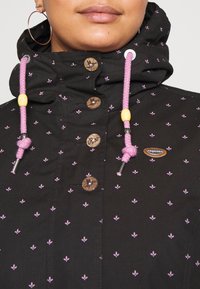 Czarna kurtka w fioletowy kwiatowy wzór. Posiada kaptur, drewniane guziki oraz różowe sznurki ze kolorowymi akcentami.