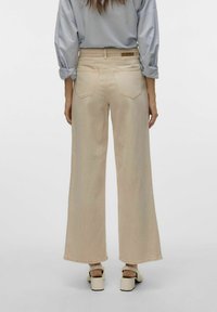 Beiga vida jeans med hög midja, fem fickor, sömnadsdetaljer och en logotyp-badge på baksidan av midjebandet. Slät denimstruktur.