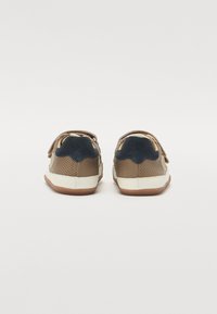 Zapatos de cuero marrón con diseño perforado, detalles en ante azul marino y suelas de goma blanca. Cintas de velcro para un fácil ajuste.
