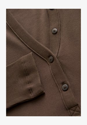 Pruun soonik, millel on V-kaelus, kuus nööpi ja rinna tasku peente detailide ja tekstuurse kangaga.