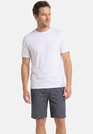 Mand iført en almindelig hvid T-shirt med korte ærmer og grå ternede shorts til knæet, stående mod en hvid baggrund.