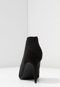Schwarze High-Heeled Stiefelette aus weichem Wildleder, mit einer glatten, geschwungenen Form und elegantem Stiletto-Absatz.