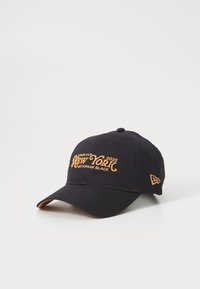 Crna kapa od pamuka s zakrivljenim vizorom. Sadrži izvezeni tekst zlatnom bojom: "Ryder Cup 2025 New York Bethpage Black" na prednjem dijelu.