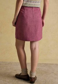 Spódnica o długości do kolan w jodełkę, w ciemnoróżowym kolorze, wykonana z teksturowanej tkaniny. Płaski pas, zaszewki z tyłu i dopasowany krój. Noszona z brązowymi butami i skarpetkami.