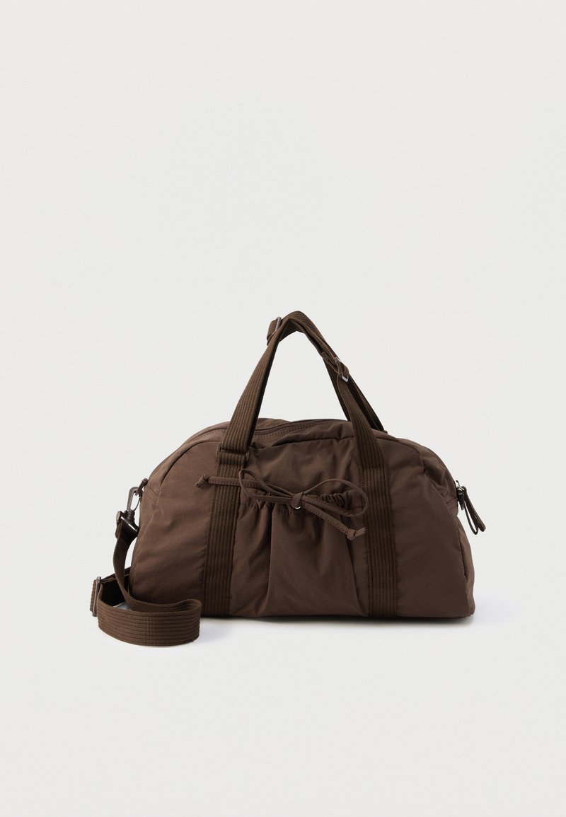 Sac de sport en tissu marron avec poignées doubles, bandoulière ajustable, poche avant plissée avec cordon de serrage, et compartiment principal zippé.