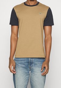 Brown and navy short-sleeve t-shirt with a crew neckline, Lacoste logo on the chest, and a soft cotton blend fabric. Straight hem.