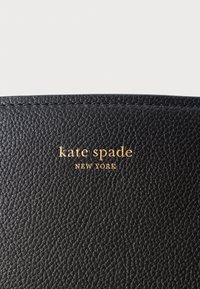 Portafoglio in pelle nera con texture, dotato di logo "kate spade NEW YORK" impresso in oro. I bordi cuciti migliorano la durabilità e il design.