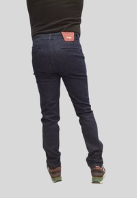 Jeans di denim scuro con vestibilità slim, dotati di un'etichetta rossa sulla cintura e due tasche posteriori. Il tessuto ha una texture liscia.