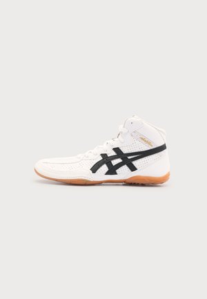 Pantof sport alb Asics cu talpă înaltă, dungi negre cu logo și talpă maro deschis pe un fundal simplu deschis.