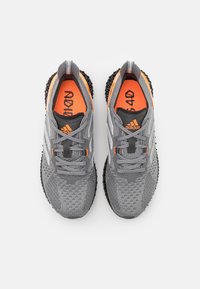 Grå träningsskor med en orange accent, med en texturerad ovandel, snörning och en hållbar svart sula med ett mönstrat design.