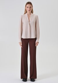 Beige Bluse mit einem abgesetzten Kragen und langen Ärmeln, kombiniert mit dunkelbraunen weiten Hosen. Glatte Textur, minimalistisches Design.