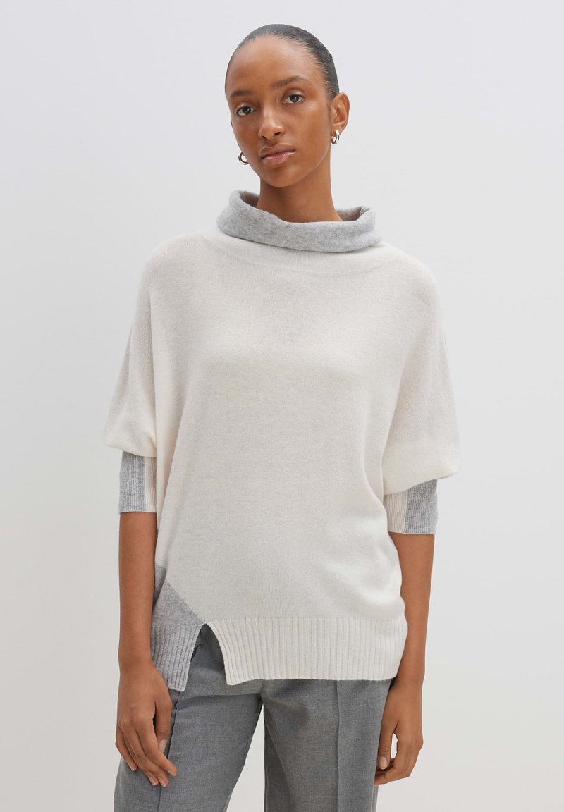 Helles Creme Oversized-Pullover mit kragen in Grau. Verfügt über kurze Ärmel mit grauen Akzenten und ein High-Low-Saumdesign. Hergestellt aus weichem Material.