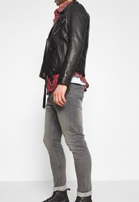 Black leather motorcycle jacket with silver zippers, worn over a red and black plaid shirt. Gray slim-fit jeans and black sneakers.