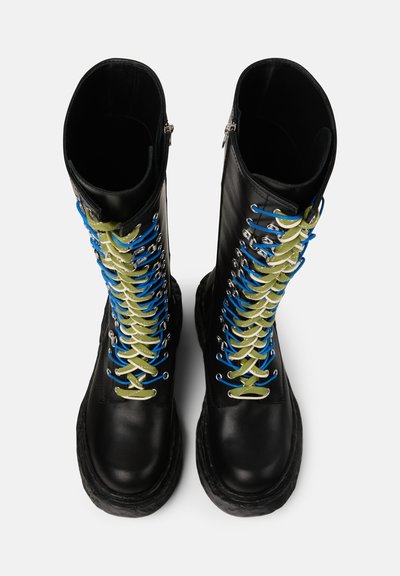 Botas de cuero negras de altura hasta la rodilla con cordones multicolores (azul, verde) y ojales plateados, con suela gruesa y cierre de cremallera.