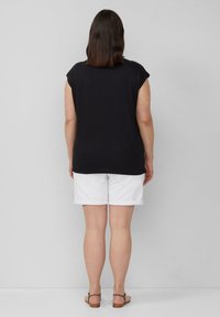 Zwarte korte mouwen top, van katoen, losse pasvorm. Gecombineerd met witte opgerolde shorts en bruine sandalen met een luipaardprint band.