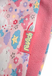 Tela colorida con un fondo rosa pastel que presenta nubes, estrellas, arcoíris y flores. Toalla de felpa rosa suave y una etiqueta roja con texto.