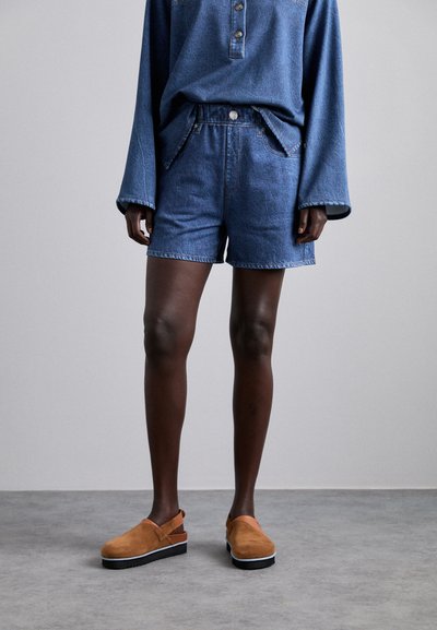 Shorts en denim de couleur bleu moyen avec une coupe décontractée, dotés d'une fermeture à bouton, de poches avant, et d'un ourlet qui se situe au-dessus du genou.