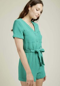 Combinaison en coton teal avec des manches courtes, décolleté en V, boutons sur le devant et une ceinture à nouer. Présente une finition texturée et deux poches avant.