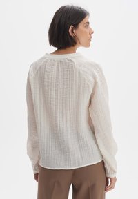 Blusa leggera, strutturata, di colore crema con maniche lunghe, scollo tondo e sottili righe verticali. Vestibilità sagomata in vita.