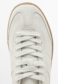 Sneaker bianco in pelle con superficie testurizzata, caratterizzato da punta rotonda, lacci piatti e suola in gomma beige. Dettagli di cucitura sottili lungo i lati.