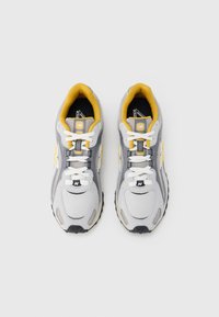 Halli, valge ja kollase värvusega New Balance jooksujalatsite paar, valgete paeltega, vaadatuna ülevalt tühi valge taust.