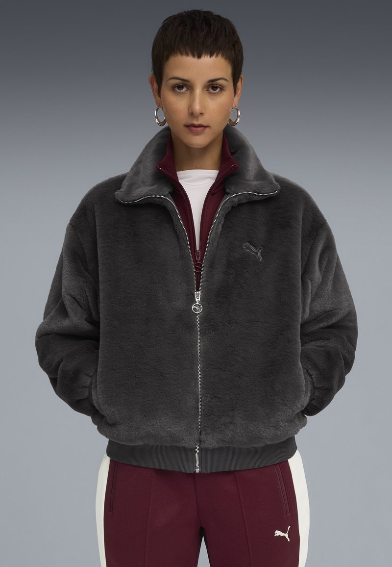 Person in gray plush zip-up jacket and maroon Puma tracksuit pants with white stripe, standing against a gray gradient background.