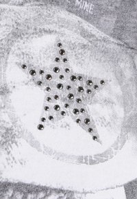 Sort og hvidt grafisk stof har en stjernesilhuet omkranset af sølvnitter, hvilket skaber et tekstureret og iøjefaldende designdetalje.