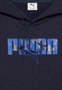 Sweat à capuche bleu marine avec "PUMA" en grandes lettres bleues remplies de motifs abstraits et un logo puma noir sautant à travers le texte.