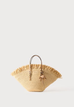 Sac cabas en paille tressée avec bord supérieur à franges, deux poignées en cuir camel avec détails de boucle, et un accessoire pompon en cuir.