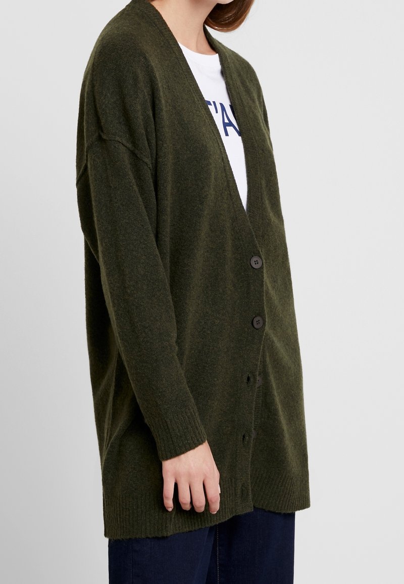 Olive green, oversized cardigan made of textured fabric, featuring a deep V-neck, button closure, and ribbed cuffs and hem.