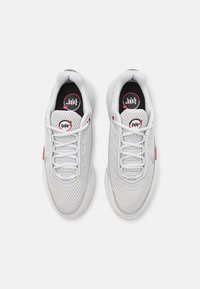 Vita mesh sneakers med en strukturerad ovansida, rund tå och en tjock sula. Har grå detaljer och en röd logotyp på tungan. Snörningsstil.