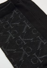 Melns audums ar atkārtotu tumši pelēku logo rakstu. Tam ir mīksta tekstūra un bezšuvju dizains. Akcentēts ar kontrastējošu maliņu.