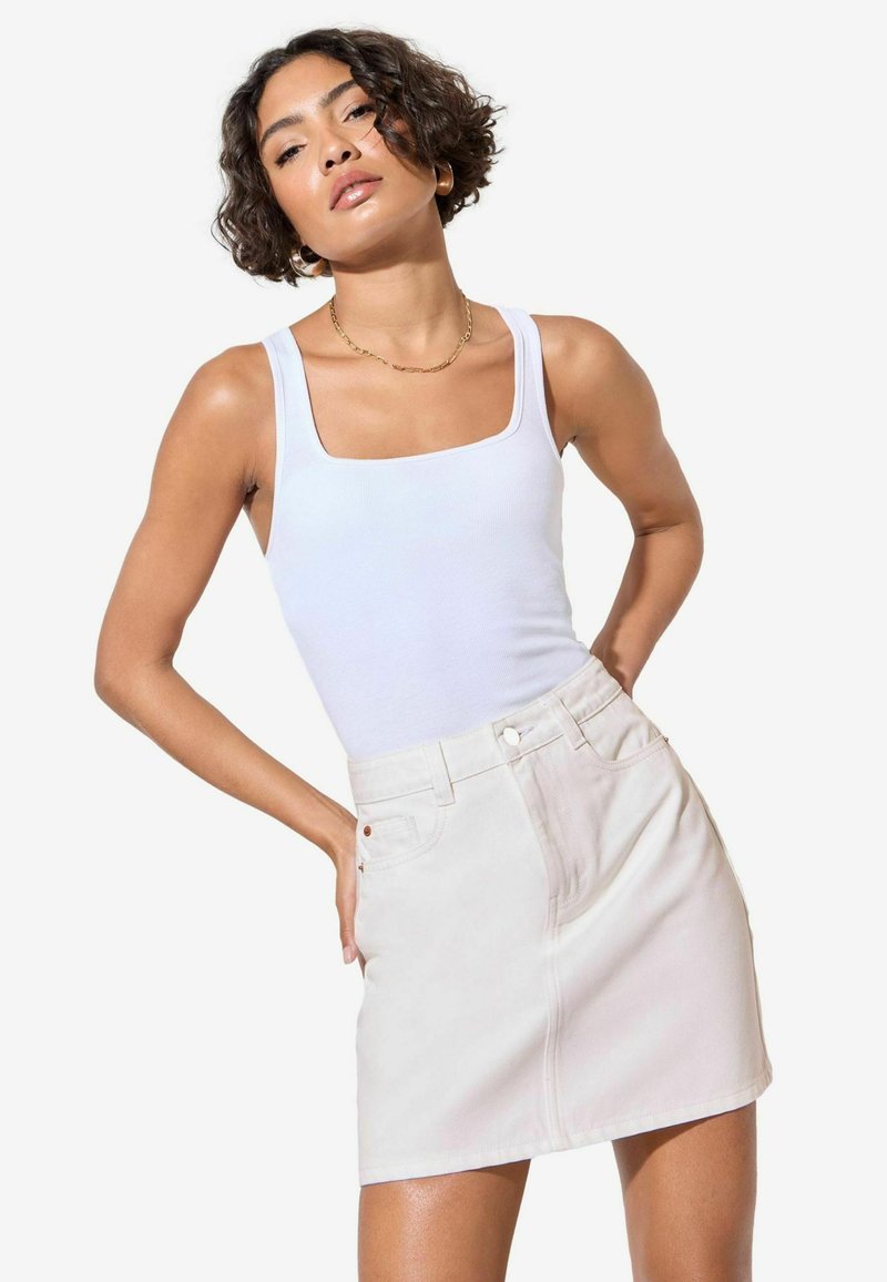 Valge tops ruudukujulise kaelusega, millele on sobitatud heledast beezist denim mini-seelik, millel on ees taskud ja diskreetne õmblusdetail.