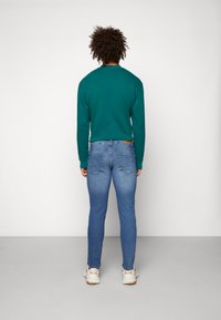 Grønn langermet skjorte kombinert med lyseblå tettsittende jeans. Sneakers og brunt lærdetalj på jeansene. Enkel design og glatt tekstur.