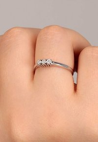 Silberring mit drei kleinen runden Diamanten, die in einem wellenförmigen Band eingesetzt sind. Der Ring hat eine glatte Oberfläche und ein schlankes, zartes Design.