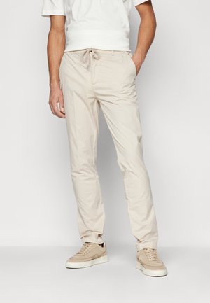 Beige chino pants with a drawstring waist, featuring a smooth texture and side pockets. Paired with light beige sneakers.