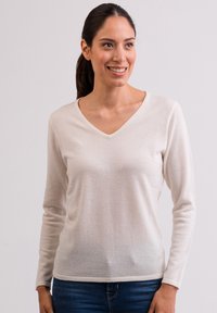 Beżowy sweter z długim rękawem w dekolcie w serek, wykonany z miękkiej, cienkiej dzianiny; charakteryzuje się prostym stylem i luźnym krojem z mankietami.