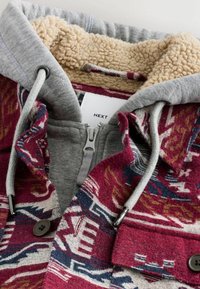 Fleeceforet jakke med et rødt og blåt mønstret ydre, grå hætte, lynlåslukning og mørke knapper. Snortræk ved hætten.