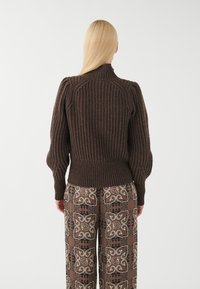 Brauner gerippter Pullover mit hohem Kragen und Puffärmeln, kombiniert mit gemusterten braunen weit geschnittenen Hosen mit aufwendigen Designs.