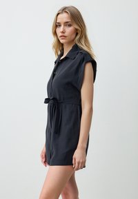 Zwarte korte mouwen romper van soepel stof, met een knoopsluiting bij de kraag, voor knopen en een tailleband voor een verstelbare pasvorm.