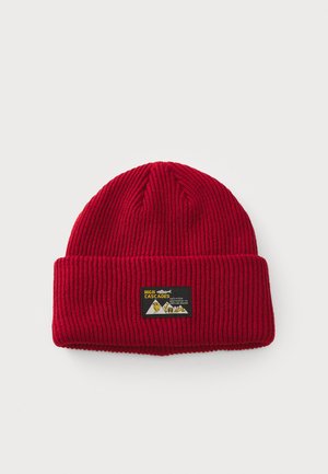 Bonnet en tricot rouge avec une texture côtelée. Présente un revers et une étiquette rectangulaire avec des montagnes et du texte sur le devant.
