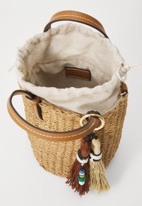 Borsa a secchiello intrecciata in paglia con manici in pelle marrone, foderata in lino beige e decorata con pon-pon nei colori marrone, crema e verde.