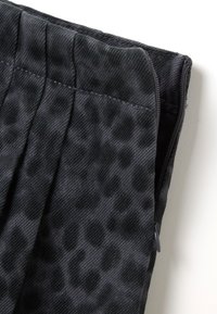 Primo piano di un tessuto nero con una sottile stampa leopardata e cuciture visibili, con una zip parzialmente aperta sul lato destro.