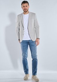 Light gray blazer made of textured fabric, paired with a white t-shirt and light blue jeans. Footwear is neutral-colored slip-on shoes.