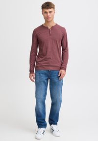 Langærmet bordaux farvet henley-skjorte med tre knapper, parret med lyseblå jeans og hvide sneakers med sorte striber. Casual pasform.