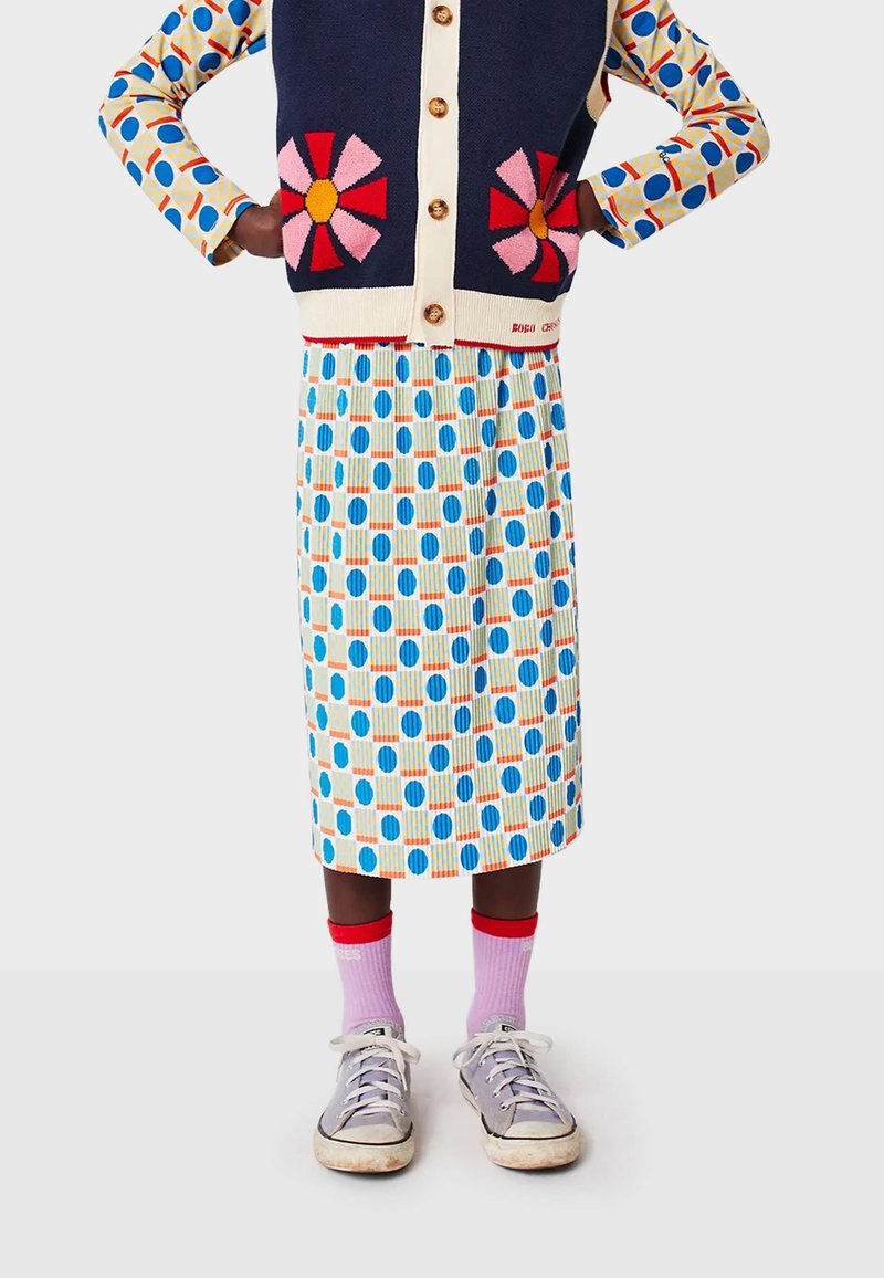 Knit cardigan with navy base, floral appliqué, and gold buttons, paired with a pleated, patterned skirt in blue, orange, and white. Gray sneakers.