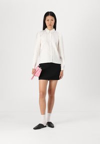 White textured blouse with a button-down collar, black skirt, and small pink handbag. Model wears black shoes and white socks.
