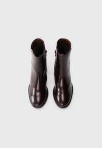Bottines en cuir marron avec une texture lisse, bout rond et design minimaliste. Équipées d'une fermeture éclair sur le côté et d'une semelle en caoutchouc basse.