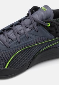 Mørkegrå atletisk sko med mesh-overdel, tekstureret overflade, sorte accenter og neongrøn detaljering langs siden og snørebåndene.